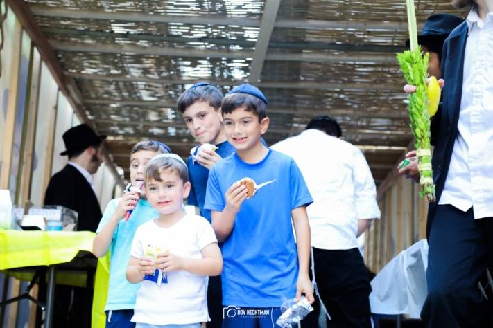 Niños en una sucá callejera, uno sostiene un lulav