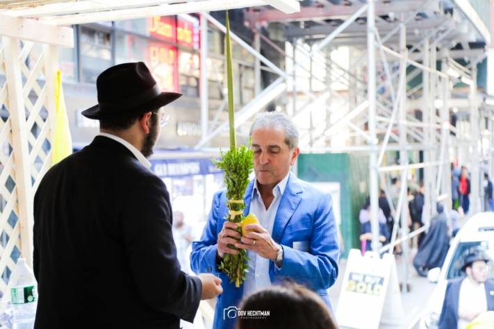 Un joven de Jabad le muestra a un visitante cómo sostener el lulav y el etrog